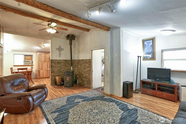 living room featuring a wood stove, beamed ceiling, rail lighting, a ceiling fan, and wood finished floors
