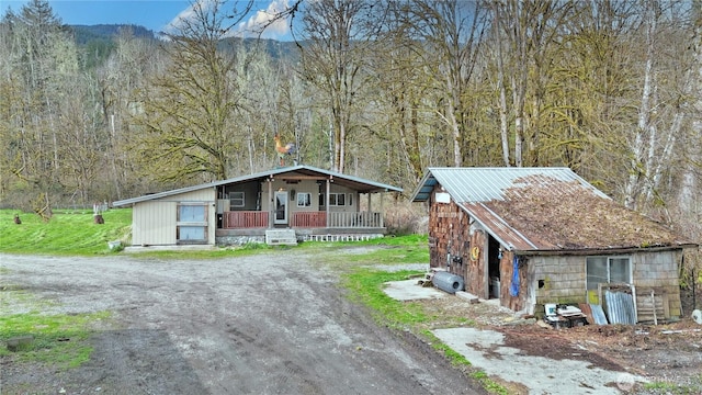 view of front of property featuring a wooded view, a porch, and an outbuilding