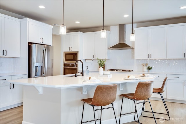 kitchen featuring white cabinets, wall chimney exhaust hood, stainless steel appliances, and a sink