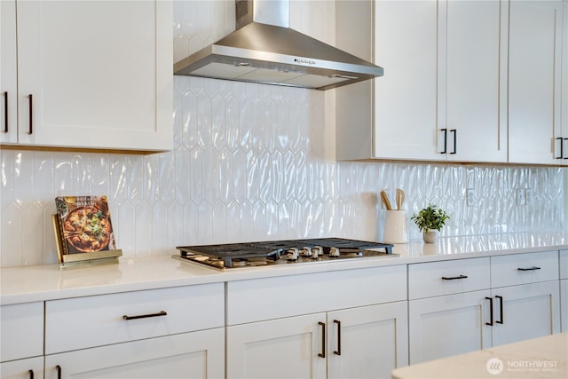 kitchen featuring white cabinets, light countertops, wall chimney exhaust hood, decorative backsplash, and stainless steel gas cooktop