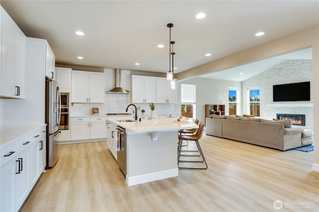 kitchen featuring stainless steel appliances, light countertops, wall chimney range hood, a sink, and light wood-style floors