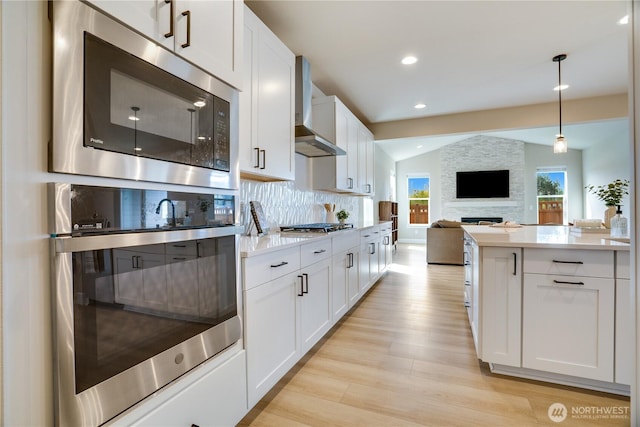 kitchen featuring light wood finished floors, stainless steel appliances, light countertops, and wall chimney range hood