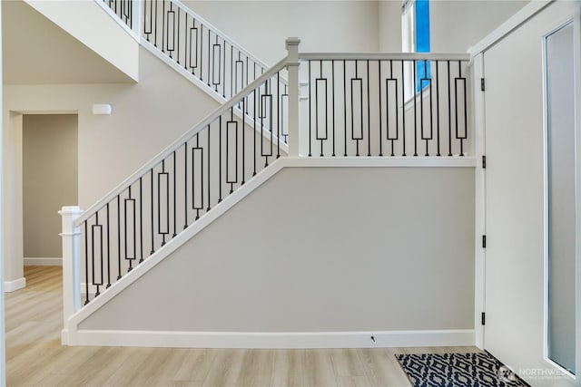 stairway featuring baseboards, wood finished floors, and a high ceiling
