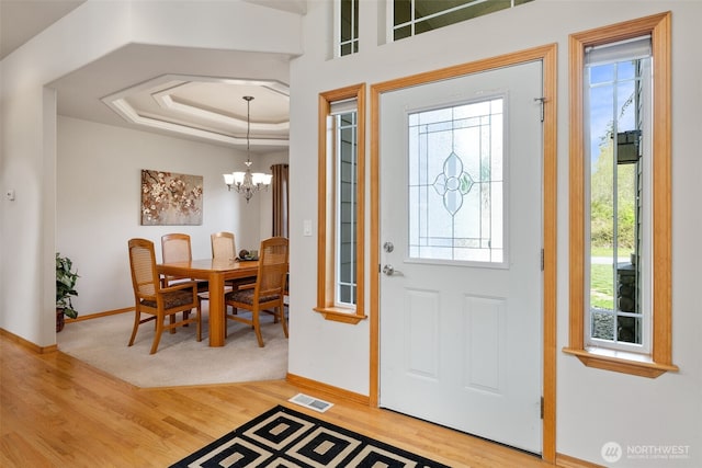 foyer entrance featuring visible vents, baseboards, light wood-type flooring, and a raised ceiling
