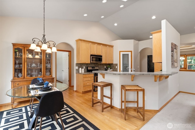 kitchen featuring arched walkways, appliances with stainless steel finishes, light brown cabinets, and a breakfast bar