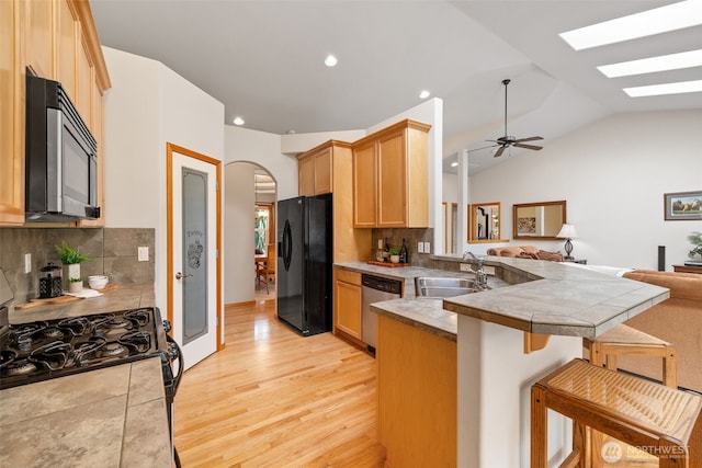kitchen with a peninsula, black appliances, a sink, open floor plan, and light wood finished floors
