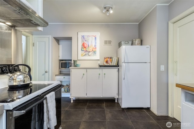 kitchen with electric range oven, freestanding refrigerator, dark tile patterned floors, white cabinets, and extractor fan