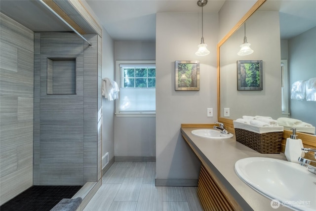 bathroom with baseboards, visible vents, a sink, and tiled shower