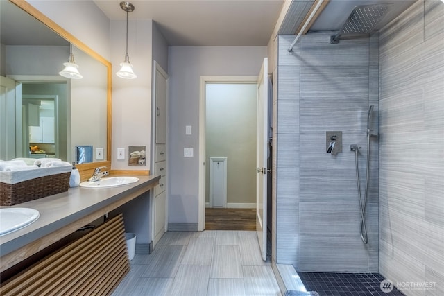 full bath featuring double vanity, a sink, baseboards, and tiled shower