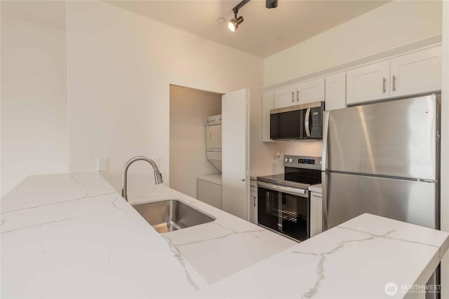 668S Lane St Unit 702, Seattle, WA 98104 - kitchen featuring stacked washer and clothes dryer, a sink, white cabinets, light stone countertops, and appliances with stainless steel finishes