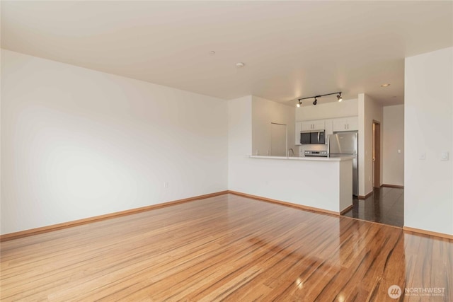 668S Lane St Unit 702, Seattle, WA 98104 - unfurnished living room with rail lighting, a sink, baseboards, and wood finished floors