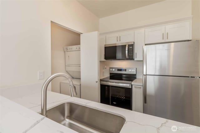 668S Lane St Unit 702, Seattle, WA 98104 - kitchen with white cabinets, light stone countertops, stacked washer / drying machine, stainless steel appliances, and a sink
