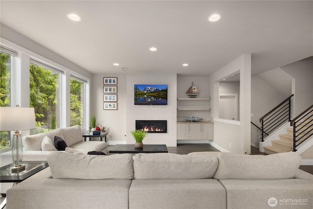 living area featuring recessed lighting, baseboards, a glass covered fireplace, stairs, and wood finished floors