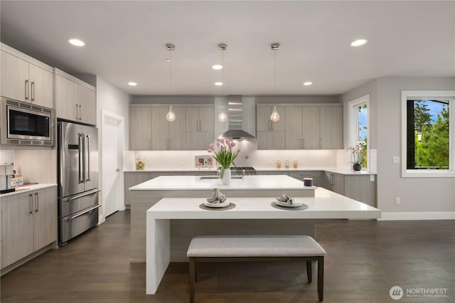kitchen featuring appliances with stainless steel finishes, wall chimney range hood, an island with sink, a breakfast bar area, and light countertops