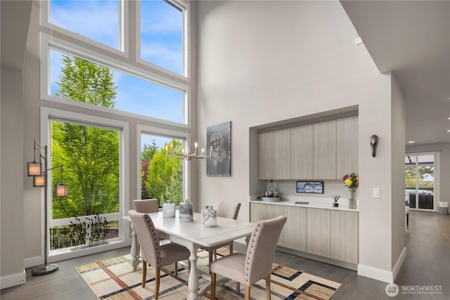 dining area featuring a towering ceiling, baseboards, and light wood finished floors