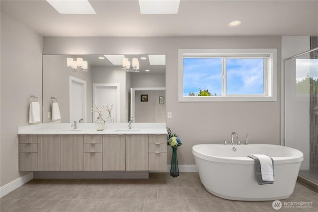 bathroom with a skylight, baseboards, double vanity, a soaking tub, and tile patterned floors