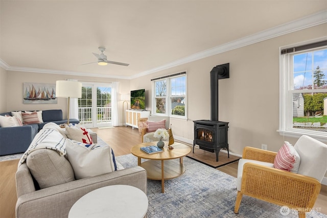 living room with crown molding, wood finished floors, a wood stove, and a ceiling fan