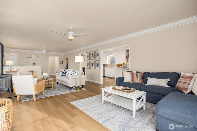 living room with baseboards, crown molding, a wood stove, ceiling fan, and wood finished floors