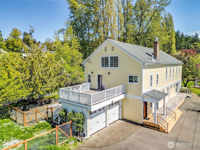 rear view of property featuring fence, driveway, a wooden deck, and a garage