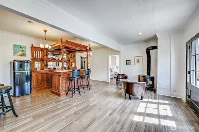 interior space with bar, crown molding, a wood stove, freestanding refrigerator, and light wood-style flooring