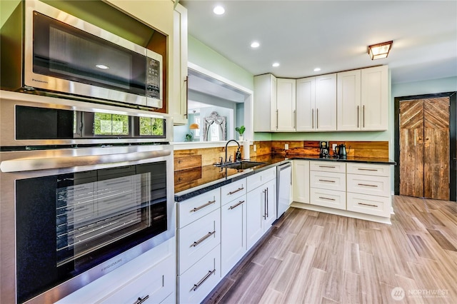 kitchen with dark countertops, recessed lighting, white cabinetry, a sink, and stainless steel appliances