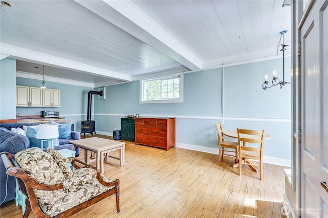 living area with baseboards, beam ceiling, light wood-style flooring, and a wood stove