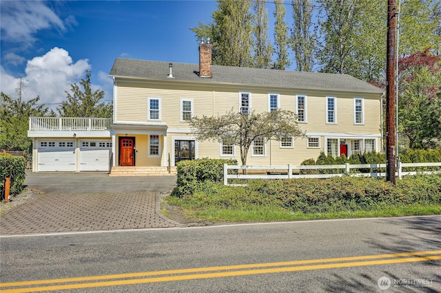 view of front facade with fence, a garage, a chimney, a balcony, and driveway