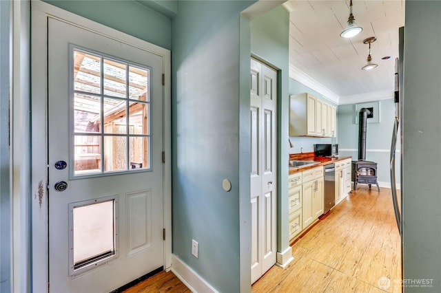 doorway to outside with ornamental molding, light wood finished floors, a healthy amount of sunlight, and a wood stove