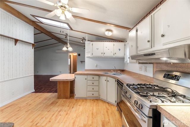 kitchen featuring wallpapered walls, under cabinet range hood, a sink, gas range, and lofted ceiling with skylight