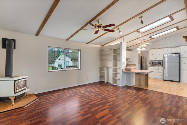 unfurnished living room with vaulted ceiling with skylight, a wood stove, a ceiling fan, and wood finished floors