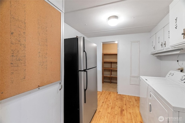 clothes washing area featuring cabinet space, washer and clothes dryer, and light wood-type flooring