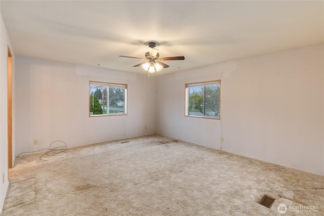spare room featuring a ceiling fan, carpet floors, a healthy amount of sunlight, and visible vents