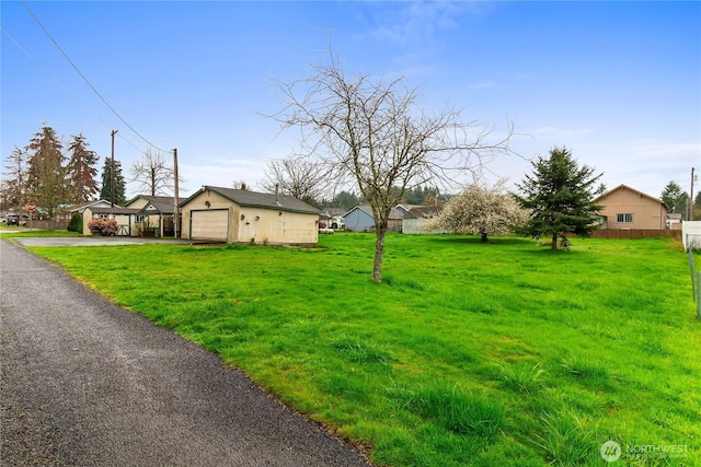 exterior space with a front lawn, a detached garage, fence, and aphalt driveway