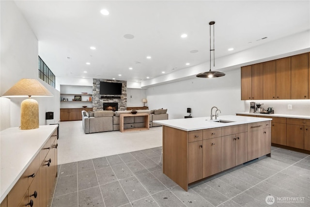 kitchen with light countertops, recessed lighting, a center island with sink, a sink, and a stone fireplace