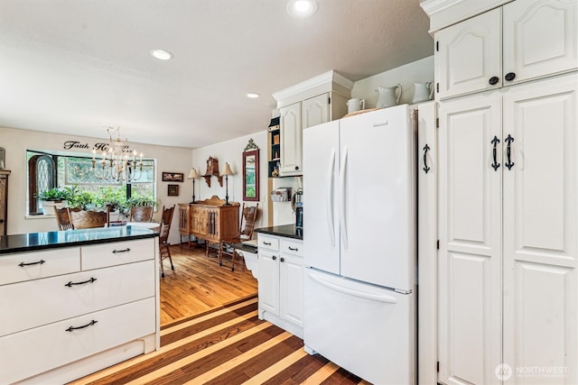 kitchen with white cabinets, dark countertops, light wood-style floors, a notable chandelier, and freestanding refrigerator
