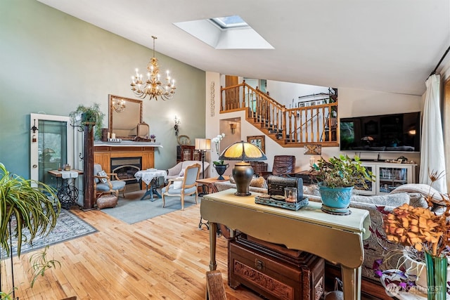 living room featuring a notable chandelier, stairway, hardwood / wood-style flooring, a skylight, and a glass covered fireplace