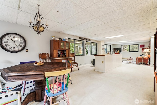 dining area featuring an inviting chandelier, light floors, and a drop ceiling