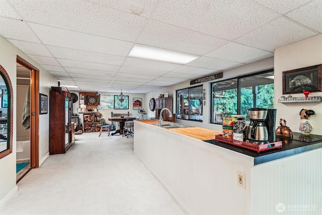 bar featuring light floors, a sink, and a paneled ceiling
