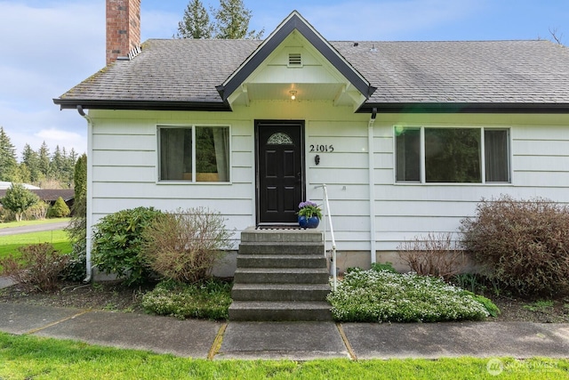 bungalow-style house with a chimney, roof with shingles, and entry steps