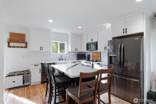 kitchen featuring white cabinets, light countertops, appliances with stainless steel finishes, a sink, and a kitchen breakfast bar