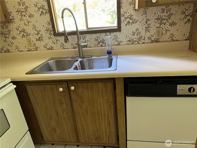 kitchen featuring white dishwasher, wallpapered walls, stove, a sink, and light countertops