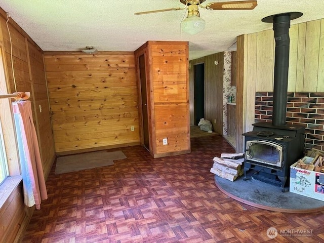 unfurnished living room with a wood stove, wooden walls, a textured ceiling, and ceiling fan
