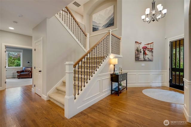 entryway with visible vents, a high ceiling, wood finished floors, stairs, and a notable chandelier