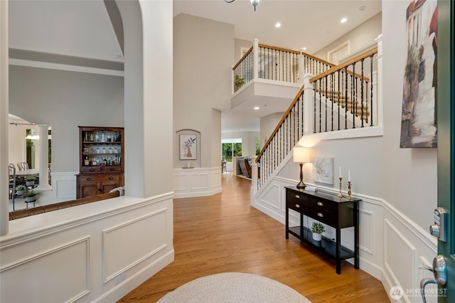 foyer entrance featuring a decorative wall, wood finished floors, a high ceiling, and stairway
