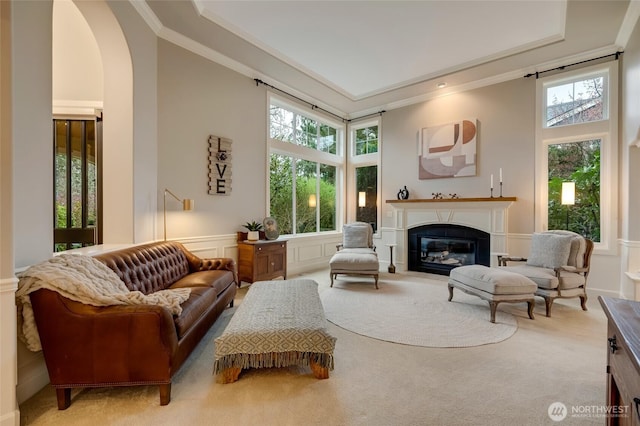 sitting room featuring a glass covered fireplace, carpet, crown molding, and a healthy amount of sunlight