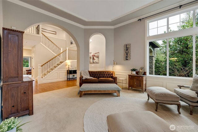 living area with arched walkways, a decorative wall, ornamental molding, stairway, and light colored carpet