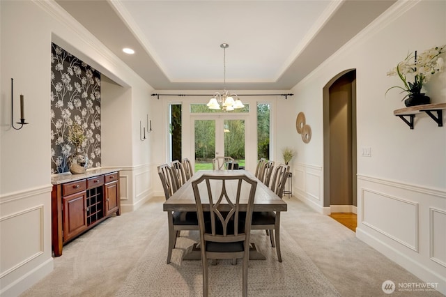 dining area featuring an inviting chandelier, french doors, a tray ceiling, a decorative wall, and light colored carpet