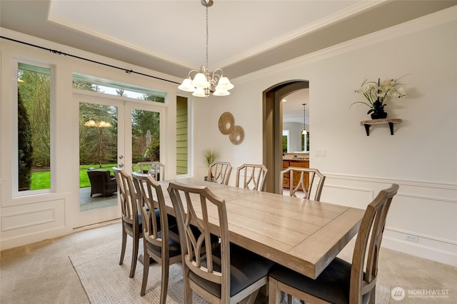 dining area with a raised ceiling, arched walkways, ornamental molding, french doors, and light colored carpet
