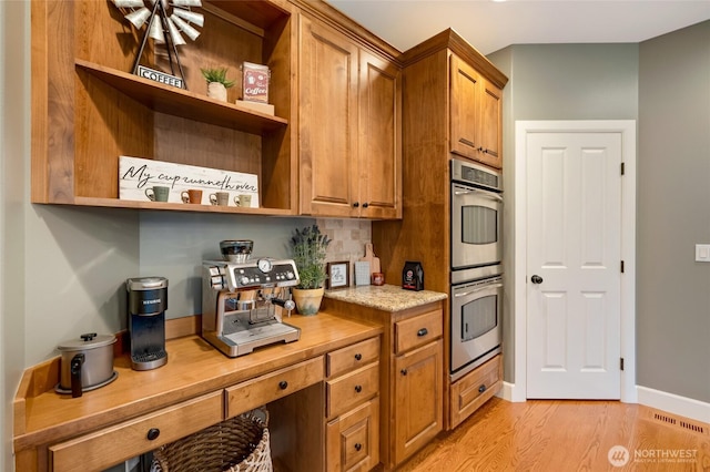kitchen featuring double oven, light wood-type flooring, open shelves, brown cabinets, and baseboards