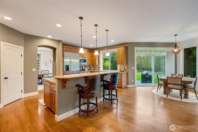 kitchen featuring light wood-style flooring, arched walkways, recessed lighting, a center island, and built in appliances